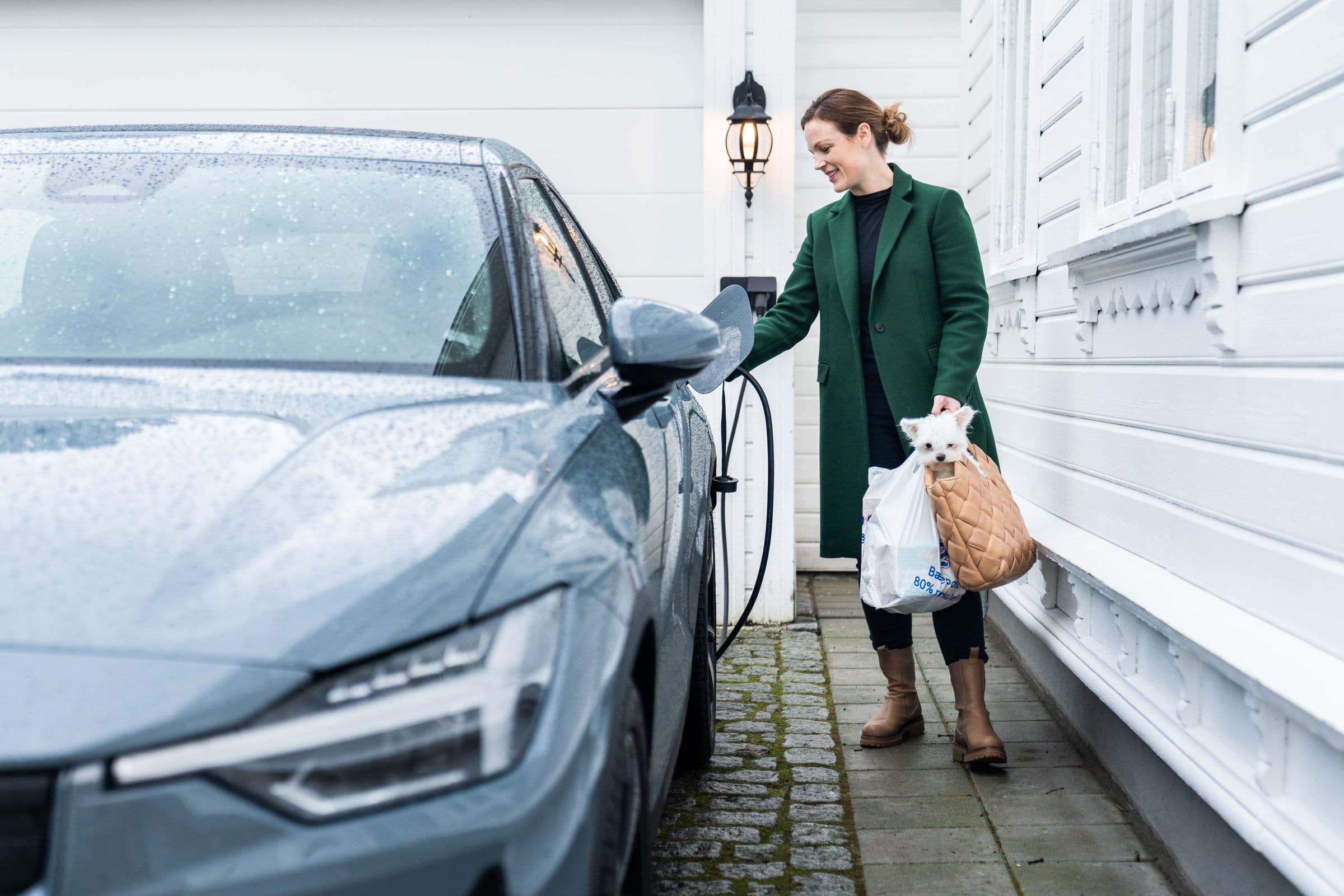 Woman charging an electric car outside a house.
